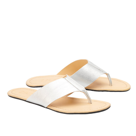 Die flachen Sandalen ZAQQ Silver mit breitem Riemen und Zehentrenner-Design heben sich elegant von weißem Untergrund ab. Die Sandalen aus Nappaleder haben eine beige Sohle mit schwarzem Rand und flexibler Sohle und bieten eine schicke und moderne Ästhetik.