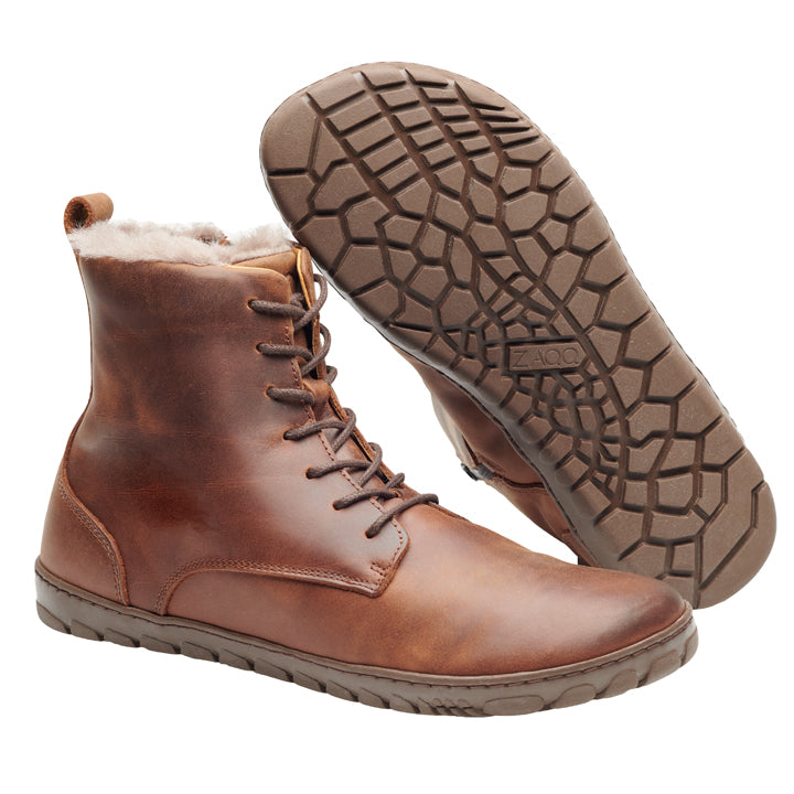 Präsentiert werden die QUINTIC Winter Antique Brown-Stiefel von ZAQQ mit Schnürung und robuster, strukturierter Sohle. Ein Stiefel steht aufrecht, um sein Seitenprofil zu zeigen, während der andere geneigt ist, um die Details der Sohle hervorzuheben. Diese Stiefel haben ein warmes Lammfell-Futter.