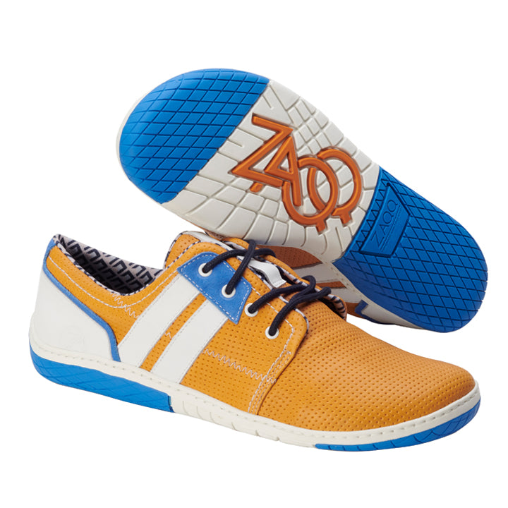 Der QAPETOWN Orange von ZAQQ besticht durch ein trendiges Design mit gelbem perforiertem Nappaleder, akzentuiert durch blaue und weiße Details und ergänzt durch blaue Sohlen. Ein Schuh liegt auf der Seite, um das geometrische Muster der ZAQQ MINIMAL-Sohle hervorzuheben, komplett mit dem orangefarbenen Logo der Marke.