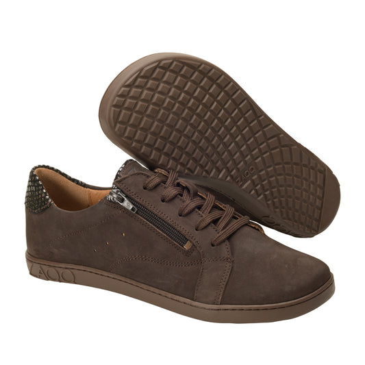 Ein Paar QOMFY Wide Dark Brown-Sneaker von ZAQQ zeichnet sich durch einen lässigen Stil mit strukturierten Gummisohlen aus Veloursleder aus. Ein Schuh steht aufrecht, um den seitlichen Reißverschluss und das Schnürdesign hervorzuheben, während der andere geneigt ist, um die gemusterte Sohle zu präsentieren. Diese Schuhe sind ideal für diejenigen, die sowohl Stil als auch Komfort schätzen.