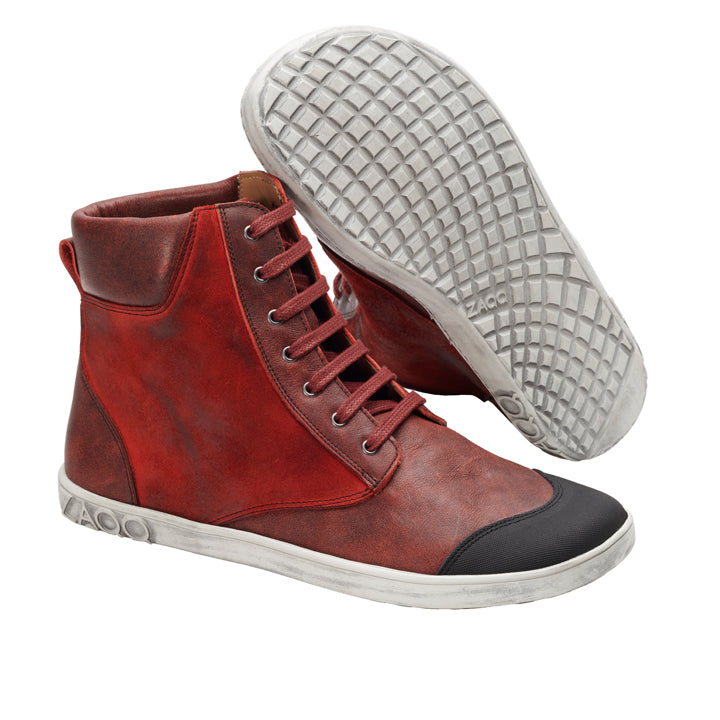 Wir präsentieren den CHICAQO Red von ZAQQ: Diese stylischen High-Top-Sneakers in leuchtendem Rot sind aus hochwertigem Nappa- und Veloursleder gefertigt. Sie haben eine glatte weiße Sohle und eine auffällige schwarze Zehenkappe. Ein Schuh steht aufrecht, während der andere geneigt ist und seine strukturierte, flexible Sohle zur Schau stellt.