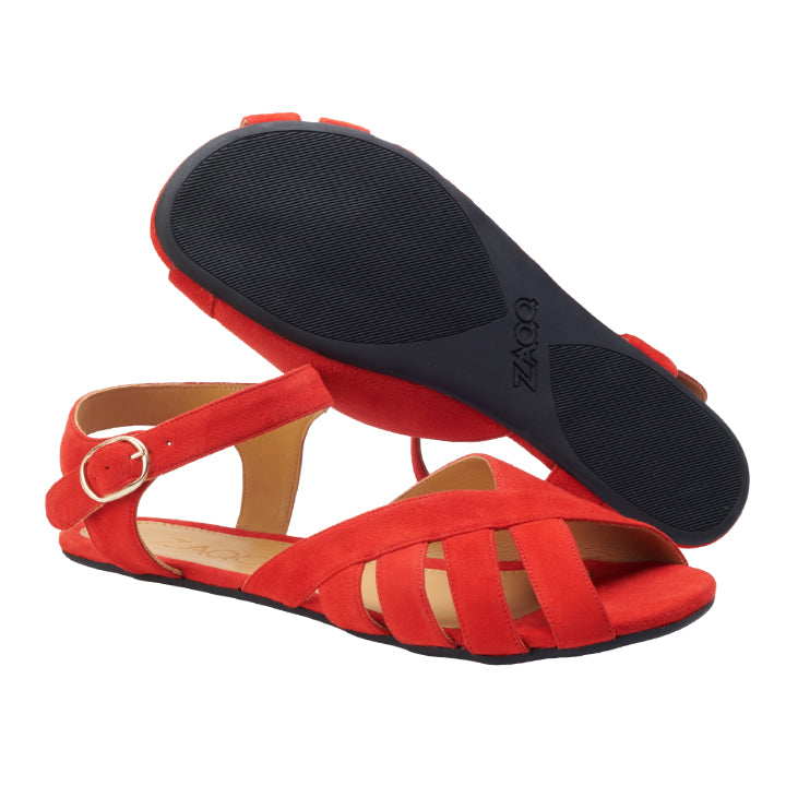 Ein Paar lebhafte rote QORSE-Sandalen von ZAQQ, wobei eine Sandale auf der Seite liegt, um den verstellbaren Knöchelriemen und das elegante Crisscross-Design aus luxuriösem Veloursleder hervorzuheben. Die andere Sandale ist umgedreht und zeigt die schwarze strukturierte Sohle, die mit einem dezenten Logoaufdruck verziert ist.