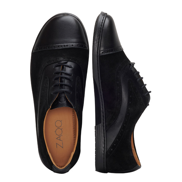 Ein Paar schwarze Oxford-Schuhe von ZAQQ QENTLE aus Nappa- und Veloursleder, wobei ein Schuh von oben und der andere von der Seite gezeigt wird. Diese Schuhe haben schwarze Schnürsenkel, ein braunes Innenfutter und tragen innen den Markennamen ZAQQ QENTLE.