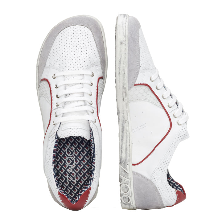 Die QLERQ White Sneaker von ZAQQ sind eine elegante Wahl und zeichnen sich durch eine Velourslederkonstruktion mit roten Akzenten aus. Diese stilvollen Schuhe verfügen über perforierte Details und ein gemustertes Innenfutter. Aus verschiedenen Perspektiven präsentiert, ist ein Schuh aufrecht positioniert, während der andere auf der Seite liegt, um die einzigartigen Designelemente hervorzuheben.