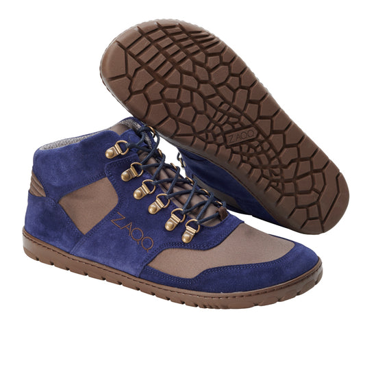 Die HIQE Mid Navy Waterproof-Schuhe von ZAQQ kombinieren blaues Wildleder mit braunen Stoffeinsätzen und sind damit die ideale Wahl für einen stilvollen Barfußschuh. Sie verfügen über braune Schnürsenkel, die durch Metallösen gefädelt sind, eine strukturierte braune Gummisohle und zeigen die Marke ZAQQ deutlich an der Seite.