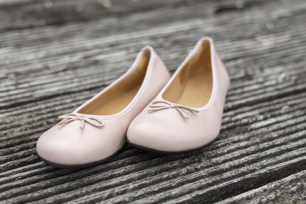 Ein Paar LOOQ Nude Ballerinas von ZAQQ, verziert mit kleinen Schleifen, ruht elegant auf einer verwitterten Holzoberfläche und zeigt ihre Mischung aus Eleganz und Komfort.