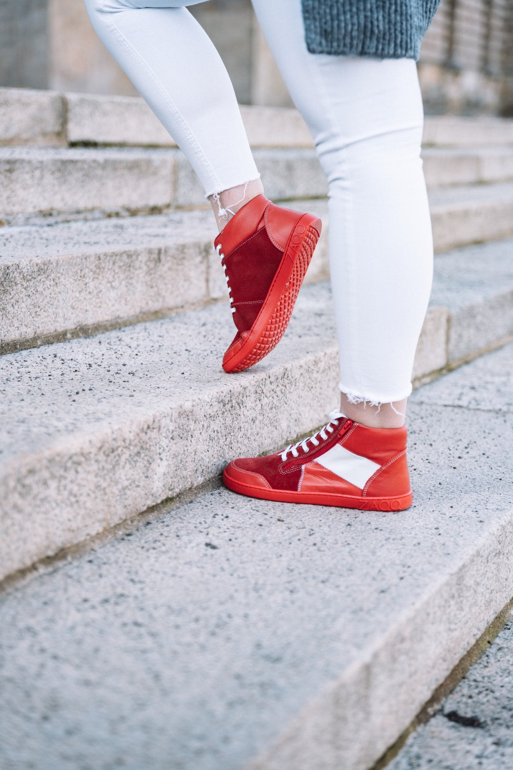 Eine Person in den High-Top-Sneakers „LUQQ Red“ von ZAQQ mit flexibler Kautschuksohle und weißen Jeans geht Steintreppe hinauf.