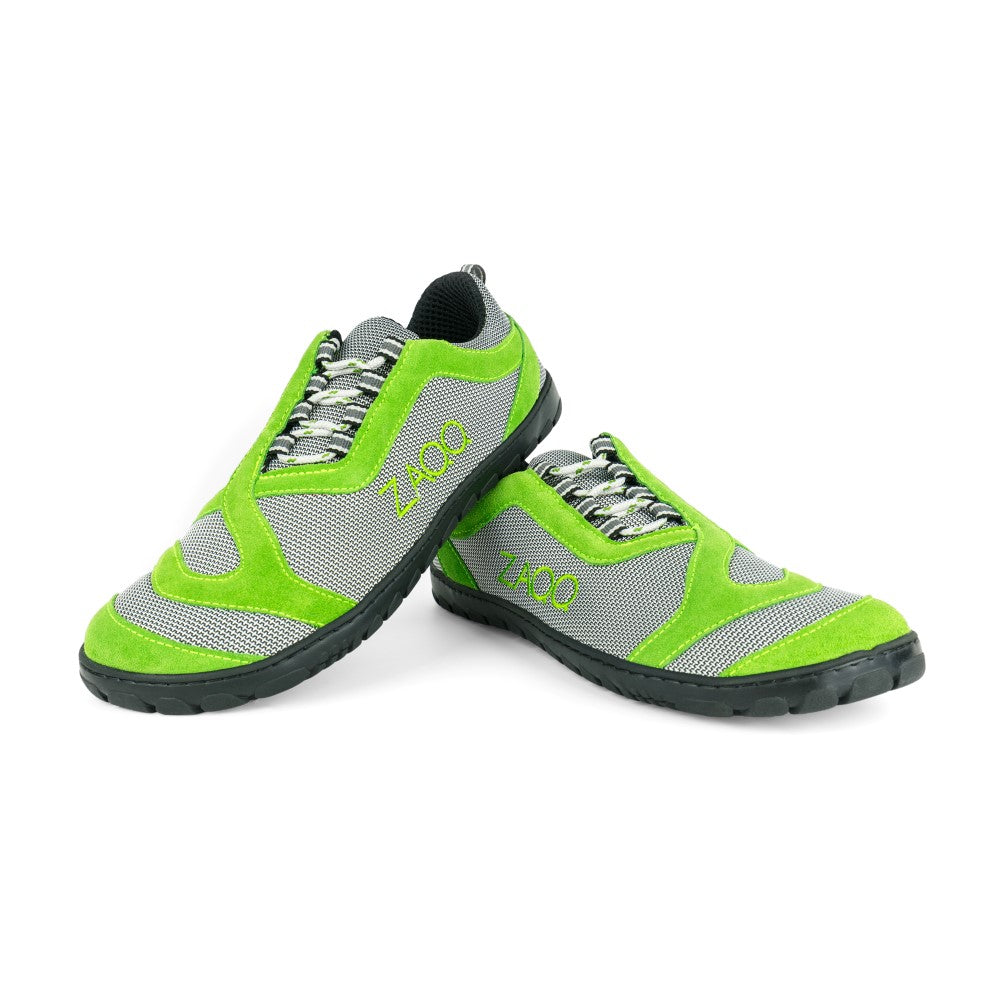 Ein Paar QUIQ Trail Green Sportschuhe von ZAQQ, die ein lebendiges Grün- und Grau-Farbschema mit Schnürung vorne und einem auffälligen Logo an der Seite vor einem weißen Hintergrund präsentieren. Diese Schuhe sind für maximalen Tragekomfort konzipiert und verfügen über robuste schwarze Sohlen, die perfekt für jedes Outdoor-Abenteuer geeignet sind. Bei dieser dynamischen Präsentation überlappt ein Schuh den anderen leicht.