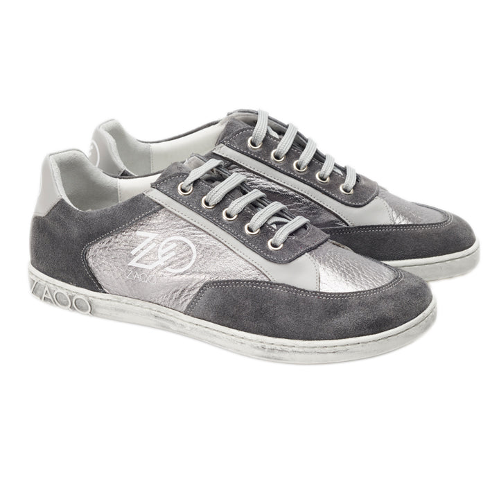 Ein Paar OQTAV Grey-Sneaker von ZAQQ, gefertigt aus samtigem Wildleder und strukturierten Einsätzen. Mit silbernen Schnürsenkeln und dem unverwechselbaren Zagoo-Logo an der Seite und der Ferse werden diese stilvollen Schuhe nebeneinander auf einem weißen Hintergrund präsentiert.