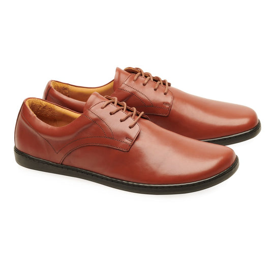 Ein Paar Oxford-Schuhe aus Cognac-Leder von ZAQQ in einem eleganten Braunton mit schwarzen Sohlen und Schnürverschlüssen. Die Schuhe sind abgewinkelt, um ihr elegantes Glattleder-Finish und die leicht spitzen Zehen hervorzuheben.