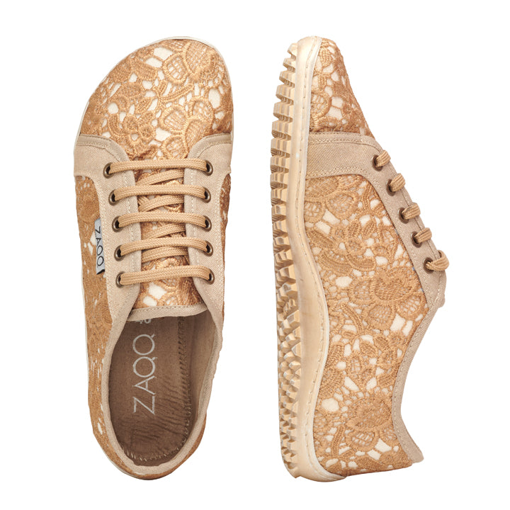 Wir präsentieren die QELLY Beige Gold-Sneaker von ZAQQ: Diese femininen Sneaker zeichnen sich durch wunderschöne Blumenmuster an den Seiten und Oberseiten aus. Ein Schuh ist von der Seite zu sehen, während der andere von oben zu sehen ist, wodurch das aufwendige Schnürsenkeldesign und die strukturierte Sohle zur Geltung kommen. Diese einzigartige Mischung aus Eleganz bietet Bewegungsfreiheit für ein unglaublich befreiendes Erlebnis.