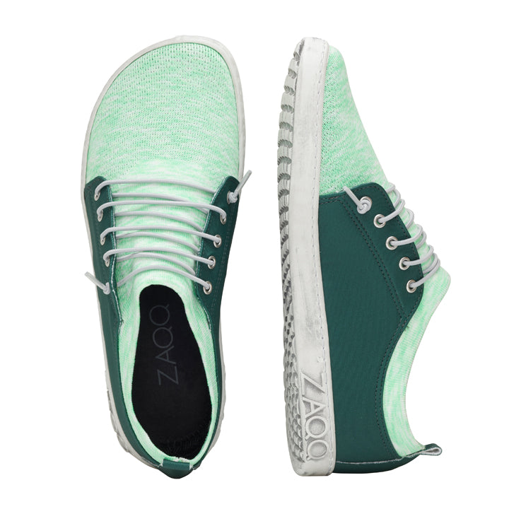 Die QRIS Green Sneaker von ZAQQ sind eine schicke Kombination aus lässiger Eleganz und präsentieren sich in einem ansprechenden Grün-Weiß-Farbschema mit weißen Schnürsenkeln. Als Barfußschuhe bieten sie mit ihrer strukturierten Sohle außergewöhnlichen Komfort. Das ZAQQ-Logo ist sowohl auf der Innensohle als auch an der Seite des Schuhs deutlich zu sehen, wobei ein Schuh aufrecht steht und der andere auf der Seite liegt.