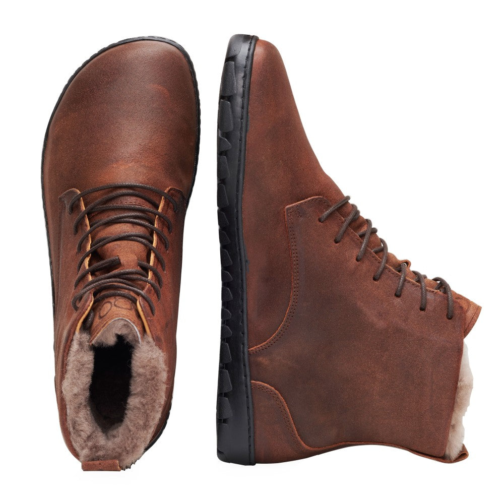 Ein Paar QUINTIC Winter Velours Brown Waterproof-Stiefel von ZAQQ, einer steht aufrecht, der andere liegt auf der Seite. Mit dunklen Schnürsenkeln, Lammfell-Futter für Wärme und schwarzen Gummisohlen mit robustem Profilmuster. Die matte Oberfläche und der leicht abgenutzte Look deuten auf wintertaugliche Strapazierfähigkeit und Stil hin.