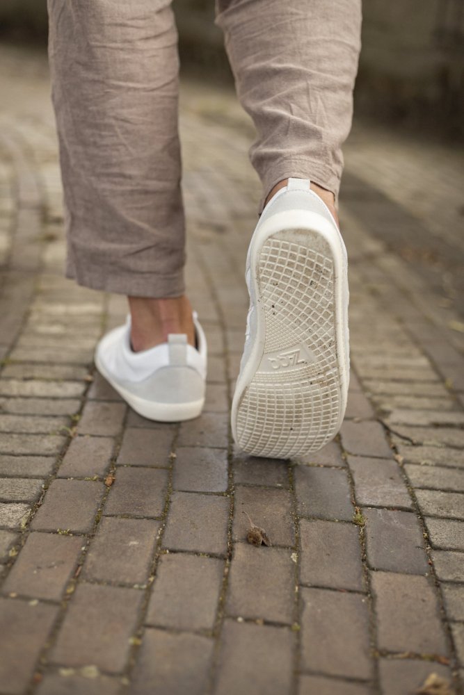 Eine Person geht in hellen Hosen auf einem Kopfsteinpflasterweg und demonstriert den Komfort des SPARQ Low White Sneakers von ZAQQ.