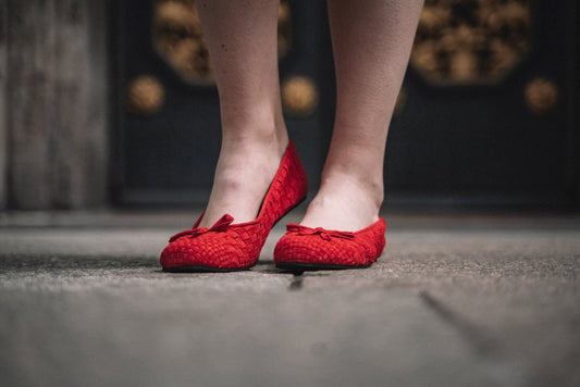 Ein Paar ZAQQ TWIST Red Ballerinas mit gewebter Textur und kleinen Schleifen auf der Vorderseite, gefertigt aus weichem Velourleder, stehen nebeneinander vor einem schlichten weißen Hintergrund.