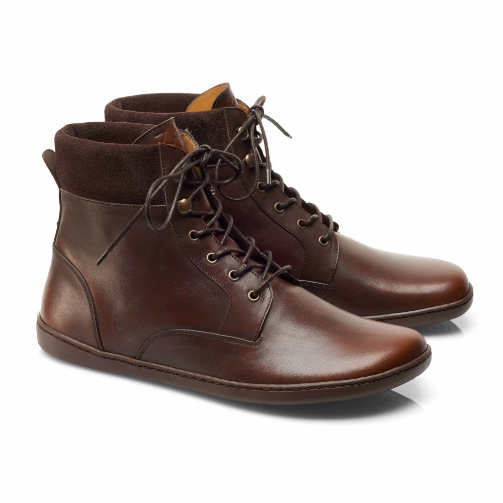 Wir präsentieren die QORBY Brown von ZAQQ, ein Paar braune Lederstiefeletten im Barfußschuh-Stil. Diese halbhohen Stiefel haben dunkle Schnürsenkel und kontrastierende Wildlederkragen und verkörpern ein schlichtes, elegantes Design mit einer flachen Sohle. Diese Stiefel kommen vor einem schlichten weißen Hintergrund perfekt zur Geltung und sind sowohl stilvoll als auch bequem.