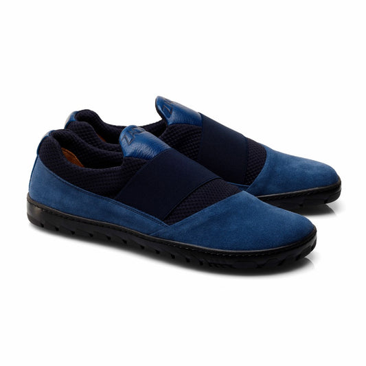 Wir präsentieren den QENT Blue von ZAQQ: ein schickes Paar sportlicher Schlupfschuh-Sneaker aus dunkelblauem Veloursleder, ergänzt durch schwarze Gummibänder und schwarze Gummisohlen, die sich alle wunderschön vor einem makellosen weißen Hintergrund abheben.