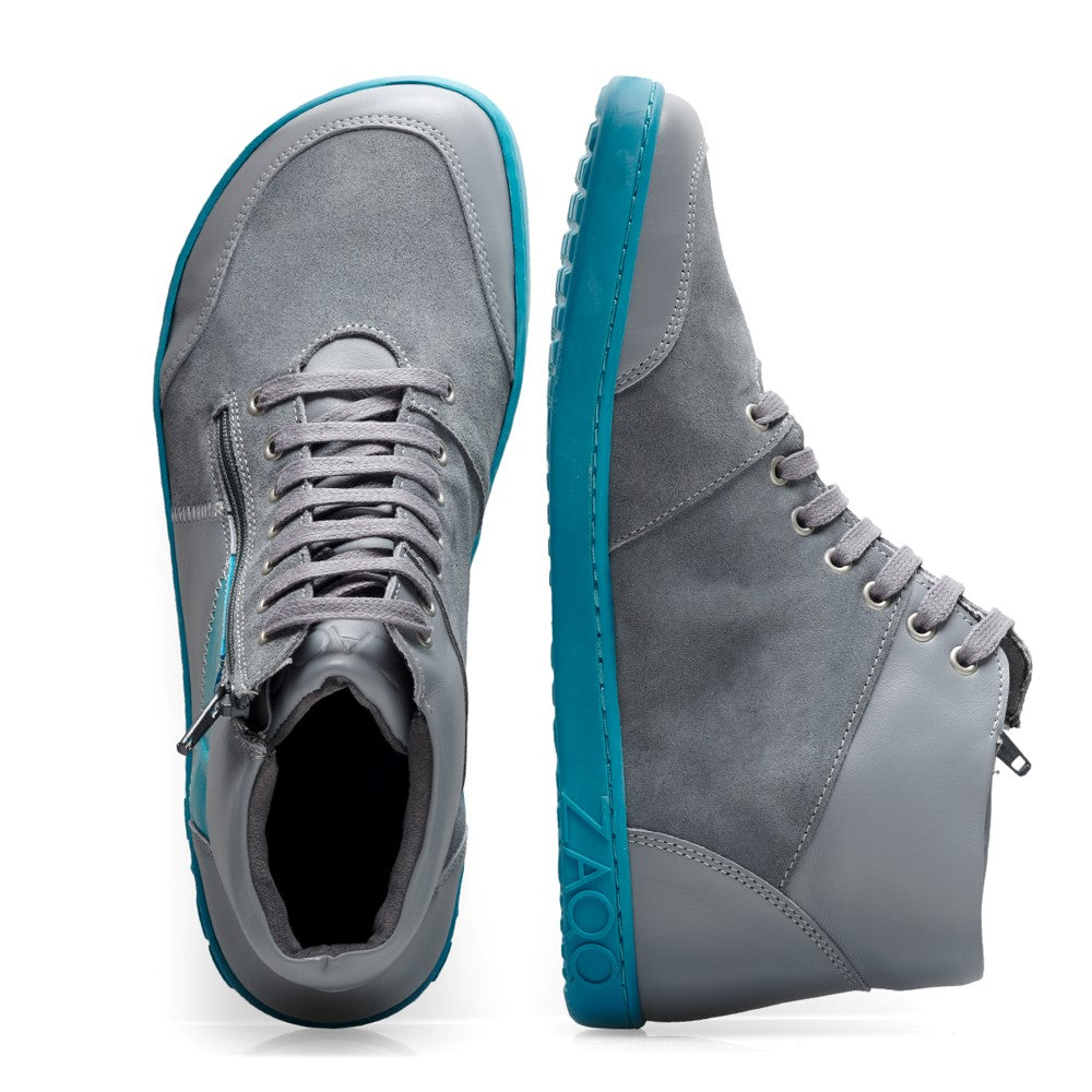 Wir präsentieren den LUQQ Turquoise von ZAQQ: Diese grauen Midcut-Sneaker haben eine leuchtend türkisfarbene Kautschuksohle. Das Design umfasst Schnür- und Reißverschlussdetails, die sich von der Seite und von oben vor einem weißen Hintergrund wunderschön präsentieren.