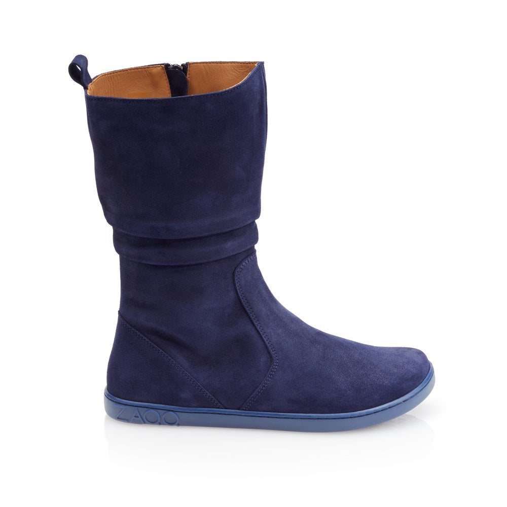 Der ZAQQ QOM Blue Single Boot präsentiert sich in marineblauem Ziegenveloursleder und einer flachen blauen Sohle mit dem charakteristischen ZAQQ Barfußsohlen-Design. Er hat eine mittlere Wadenhöhe, einen lässigen Schnitt, einen seitlichen Reißverschluss und eine Schlaufe für bequemes Tragen, zusammen mit einem geprägten Markenlogo in der Nähe der Ferse und einer hellbraun gefütterten Innenseite.