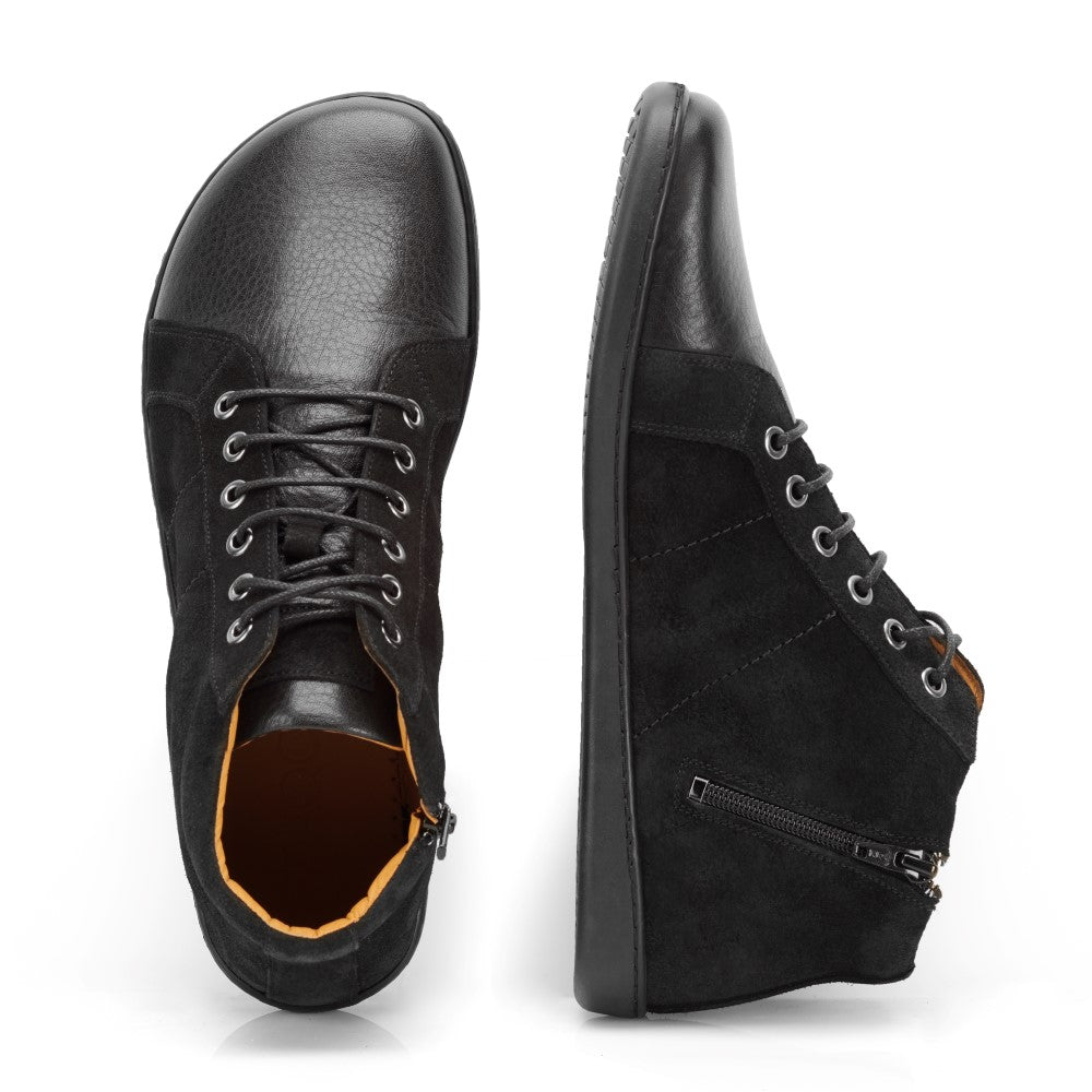 Die ZAQQ QORE Mid Black High-Tops sind aus schwarzem Leder gefertigt und verfügen über Schnürsenkel und seitliche Reißverschlüsse. Ein Schuh, der einem minimalistischen Sneaker ähnelt, wird von oben präsentiert, wodurch die Zehenpartie und die Schnürsenkeldetails hervorgehoben werden, während der andere Schuh von der Seite präsentiert wird, um die Reißverschluss- und Nähdetails hervorzuheben.