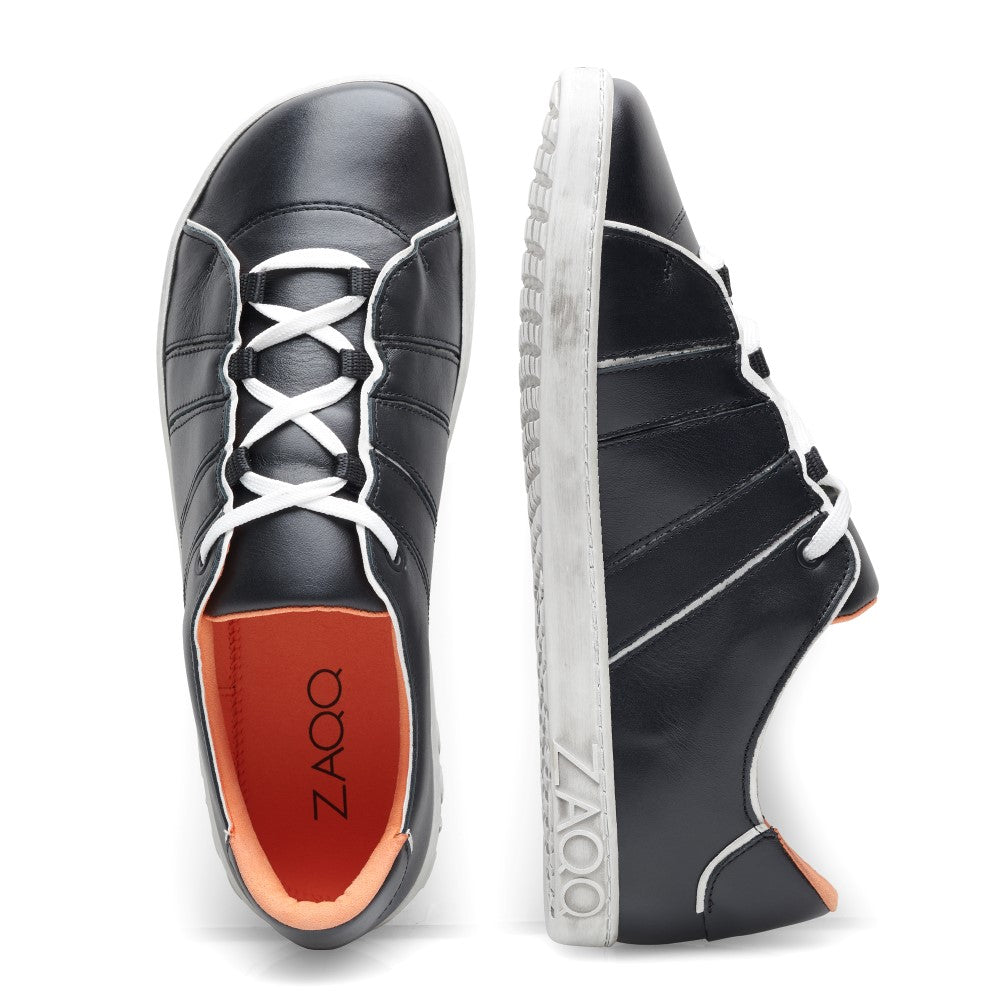 Die QQQ Low Black White Sneaker von ZAQQ zeichnen sich durch ein elegantes schwarzes Lederdesign mit weißen Sohlen und Schnürsenkeln aus. Ein Schuh ist von oben zu sehen und zeigt seine rote Innensohle und das markante ZAQQ-Branding, während der andere von der Seite zu sehen ist und sein stilvolles Design und seinen Komfort hervorhebt.