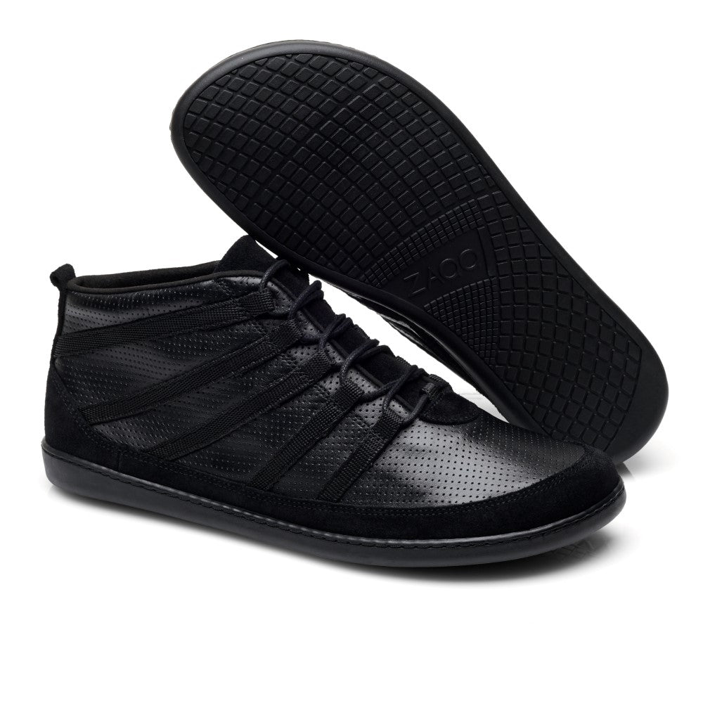 Die SPARQ Mid Black Sneaker von ZAQQ sind elegante High-Tops aus Nappaleder mit Lochmuster und Vollgummisohle. Ein Schuh liegt flach, der andere liegt auf der Seite, was ein ultramodernes Design unterstreicht und gleichzeitig die strukturierte Sohle zur Geltung bringt.